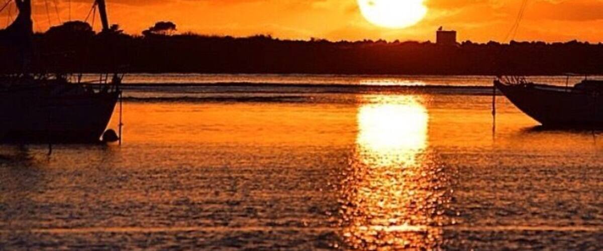 A sunset over a calm body of water with two boats and a bird in the sky.