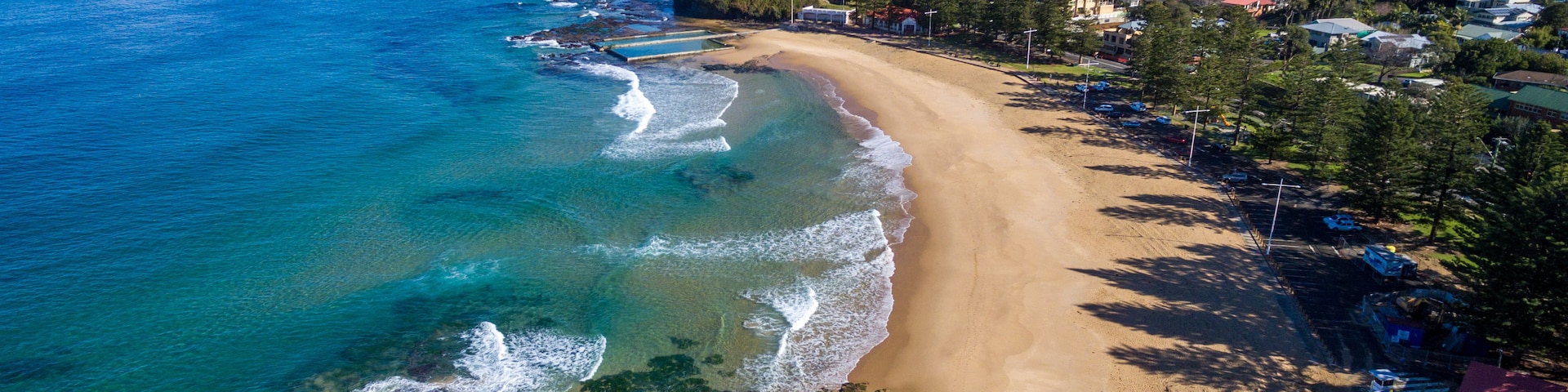 Une ville côtière dotée d’une plage de sable, d’eaux bleues et limpides, et bordée de collines.