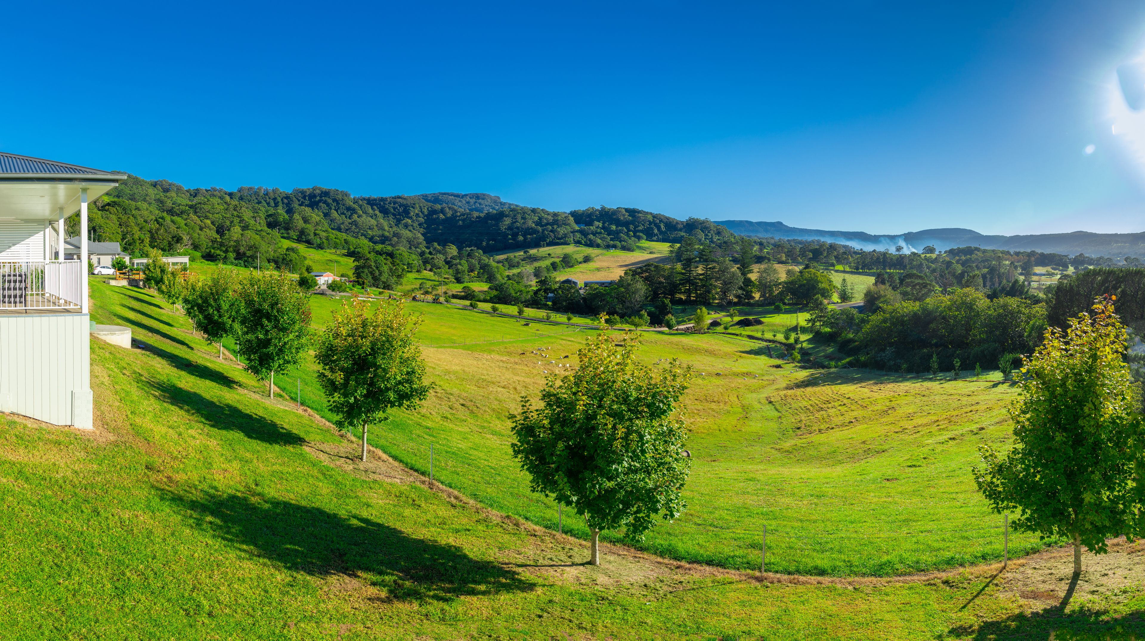 A lush green valley with rolling hills, a white building on the left, and a clear blue sky.