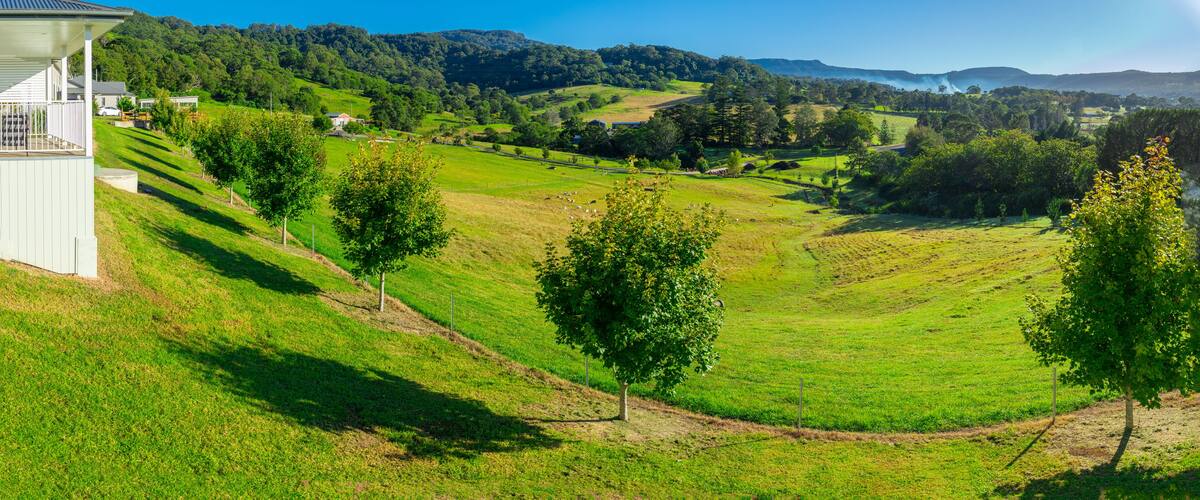 A lush green valley with rolling hills, a white building on the left, and a clear blue sky.