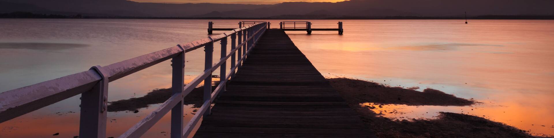 A wooden pier extending into a calm body of water with a sunset sky.