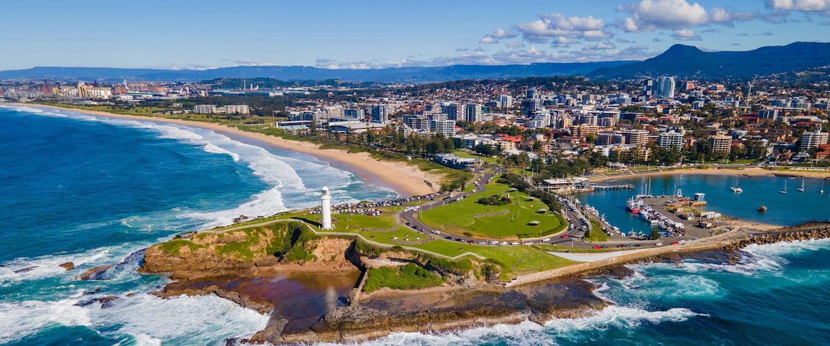 A coastal cityscape with a lighthouse, beach, and marina.