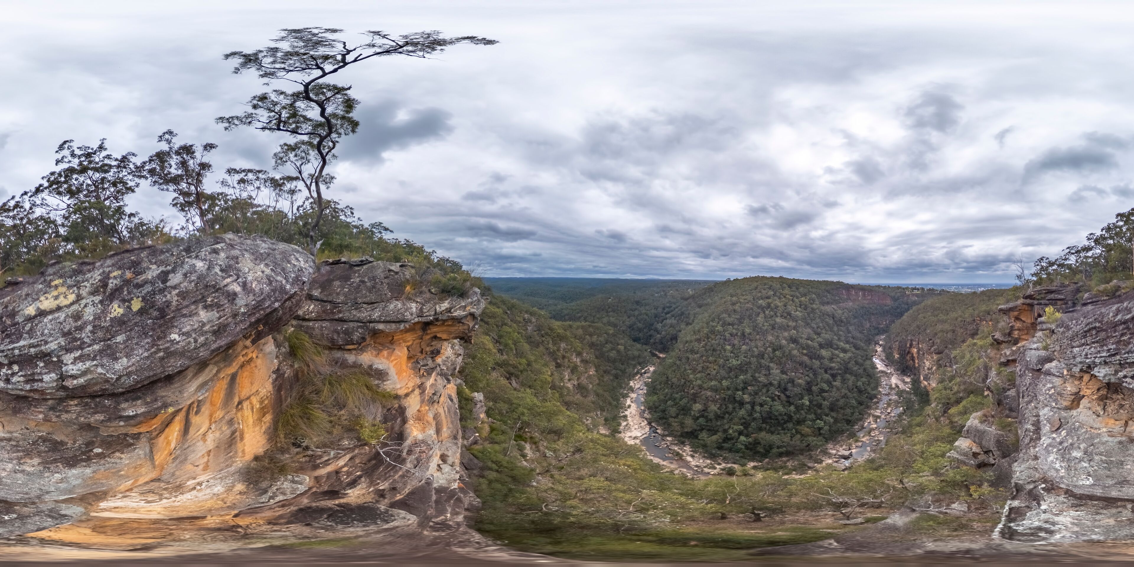 A rugged cliff with a river flowing through a valley surrounded by dense forest.