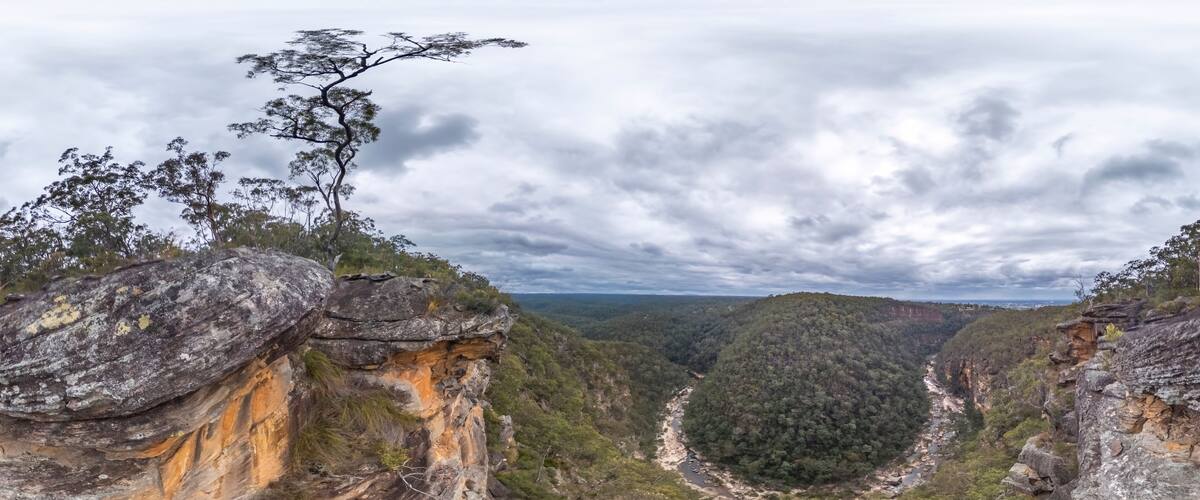 A rugged cliff with a river flowing through a valley surrounded by dense forest.