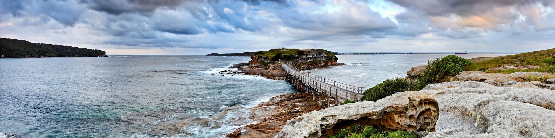 A coastal landscape with a rocky shoreline, a wooden pier, and a distant ship on the horizon.