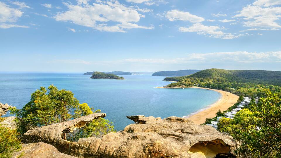 A coastal landscape with a beach, rocky outcrops, and distant islands.