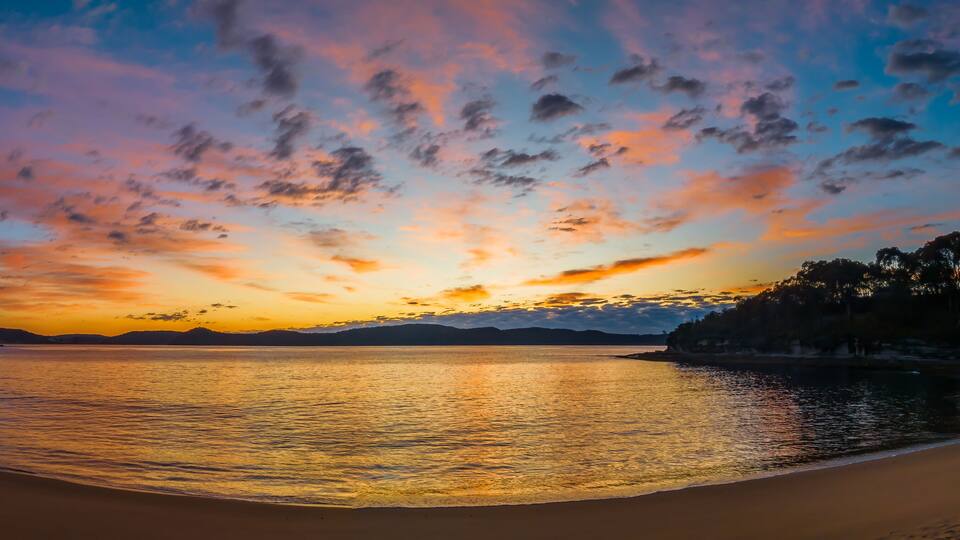 A beach at sunset with a clear sky and calm water.
