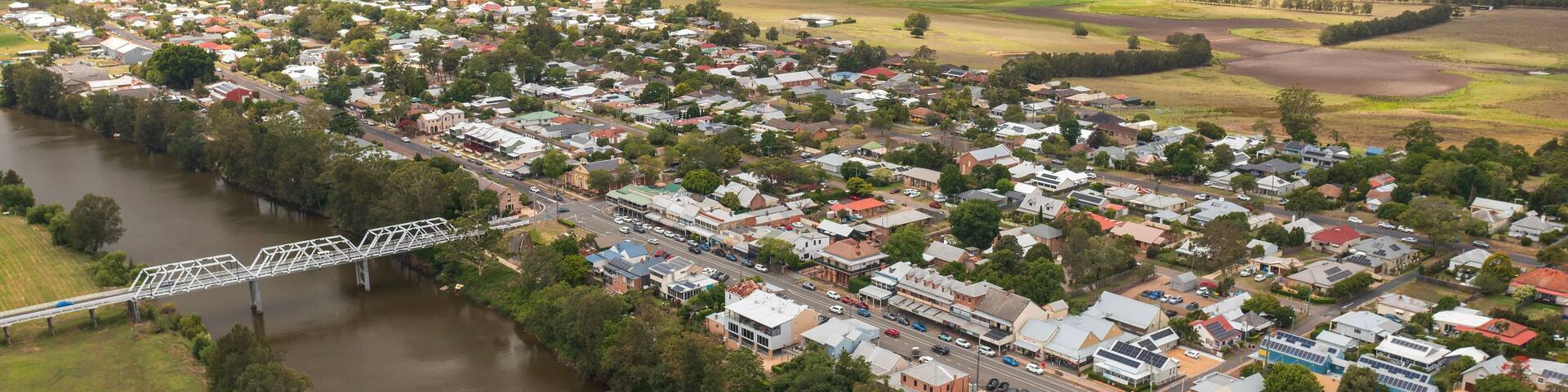 An aerial view of a riverside town with a bridge, houses, and surrounding fields.