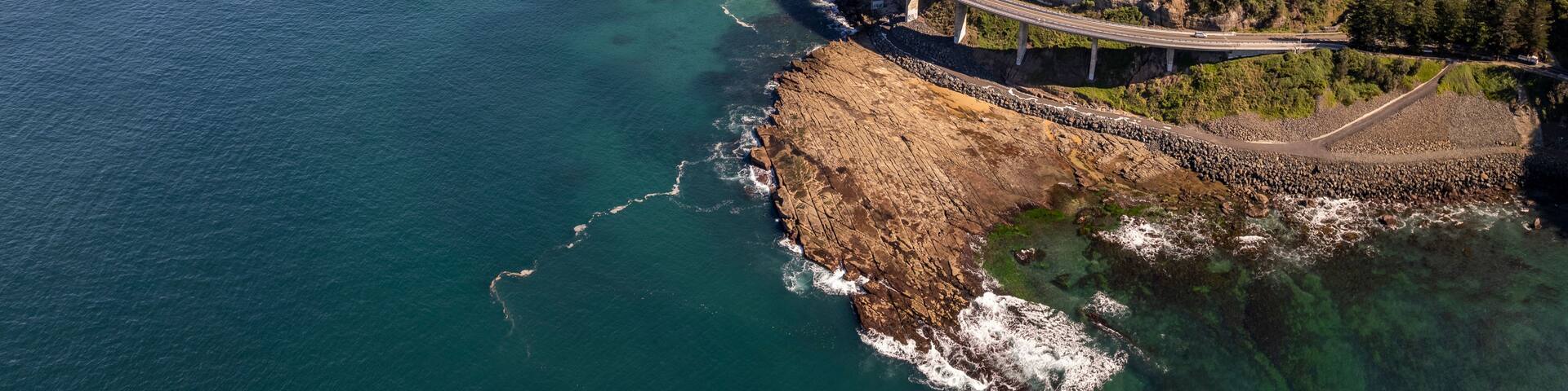 A coastal road with a bridge spanning a rocky cliff over the ocean.