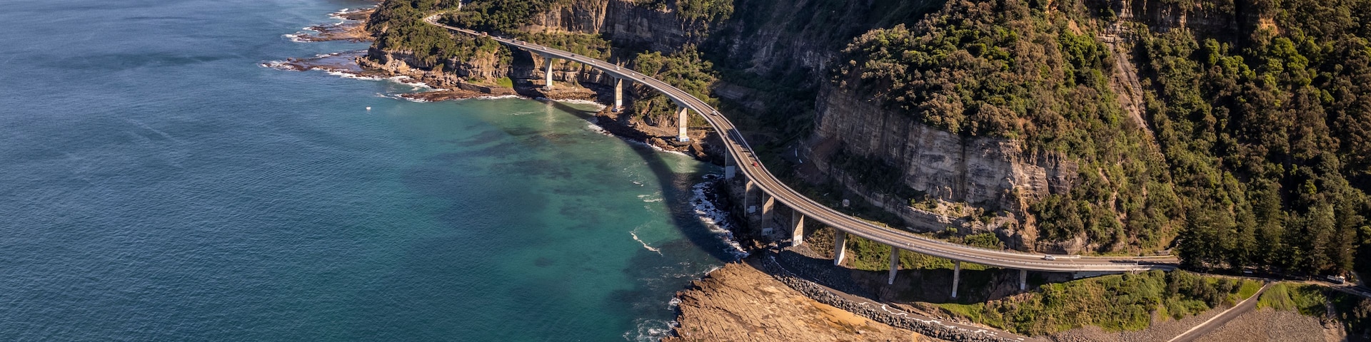 Uma estrada costeira com uma ponte sobre um penhasco rochoso, com vista para o oceano.