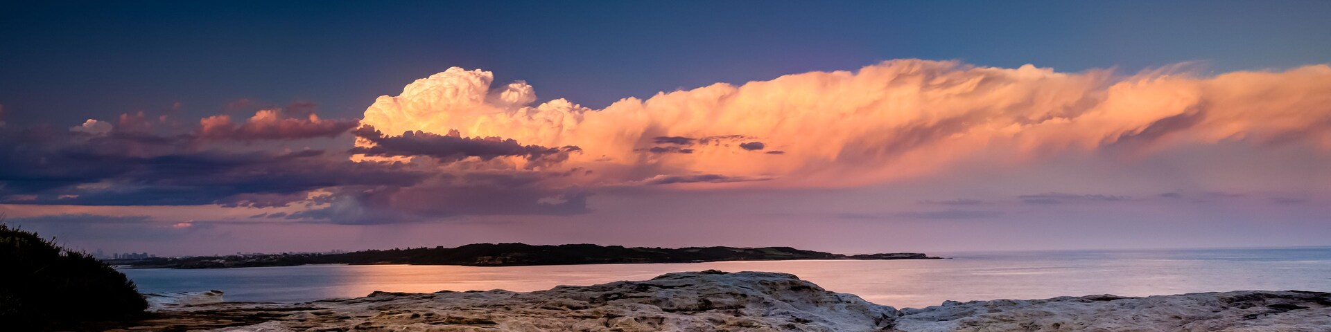 A coastal landscape with a large body of water, rocky terrain, and a dramatic sky with clouds reflecting on the water's surface.
