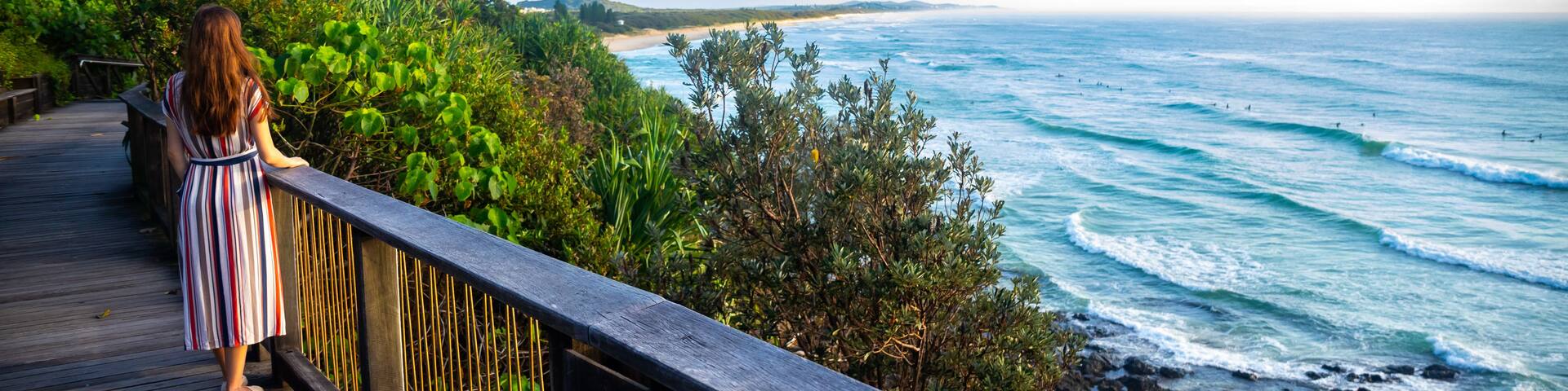 A woman on a wooden boardwalk overlooking a beach with waves.