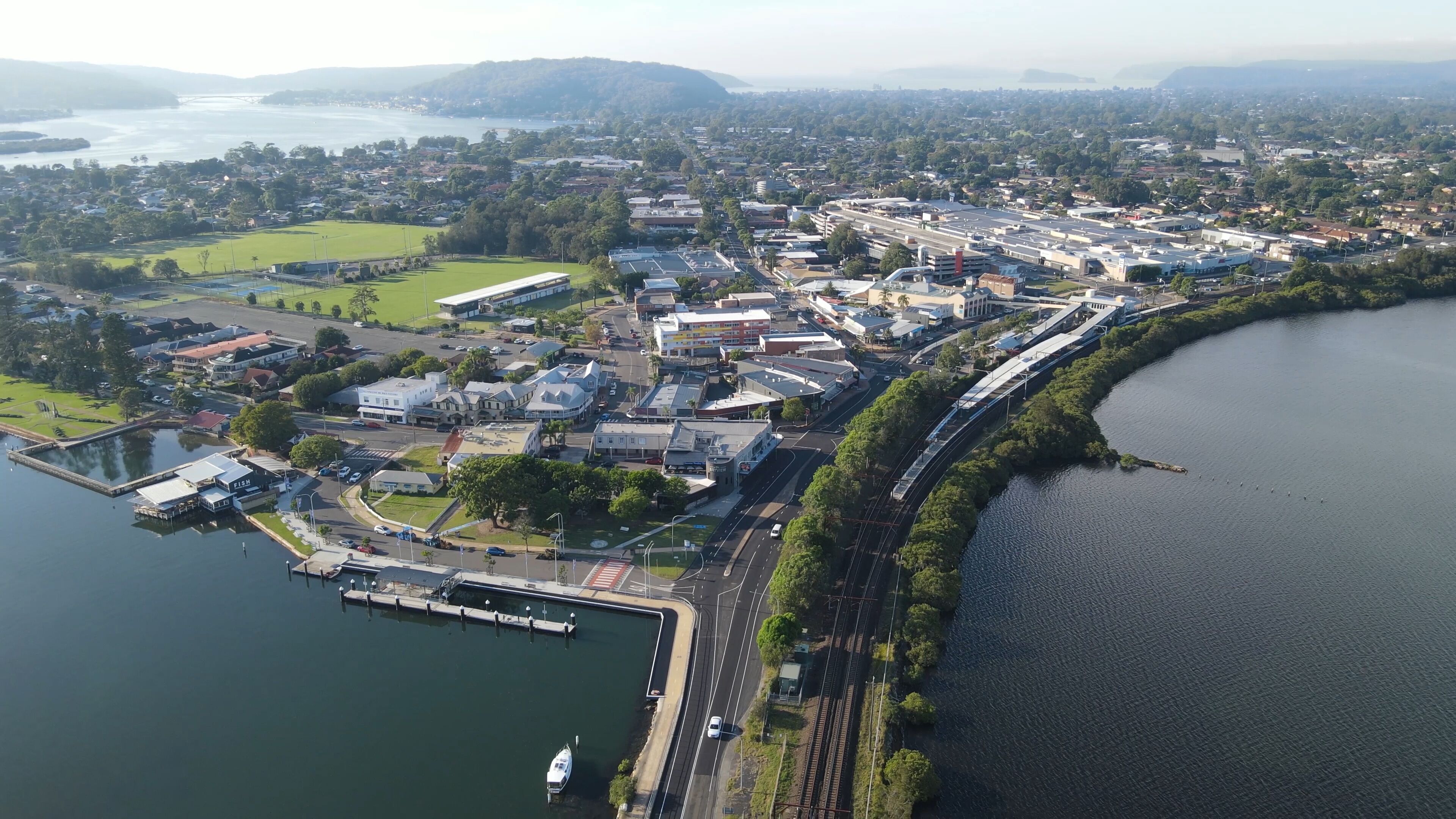 An aerial view of a lakeside town with a marina, a train line, and surrounding greenery.