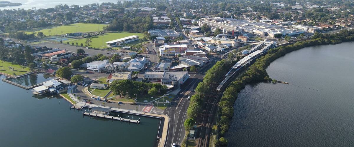 An aerial view of a lakeside town with a marina, a train line, and surrounding greenery.