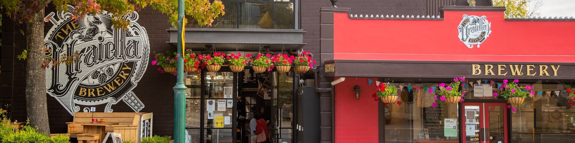Una cervecería con fachada roja y macetas colgantes de flores.