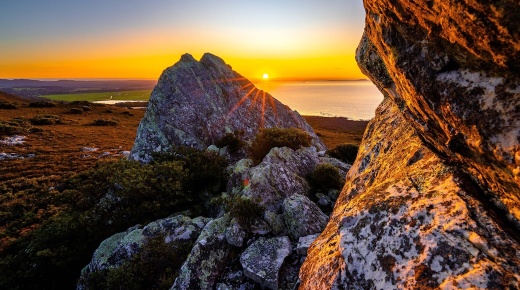 A sunset over a coastal landscape with prominent rock formations and a distant view of the sea.