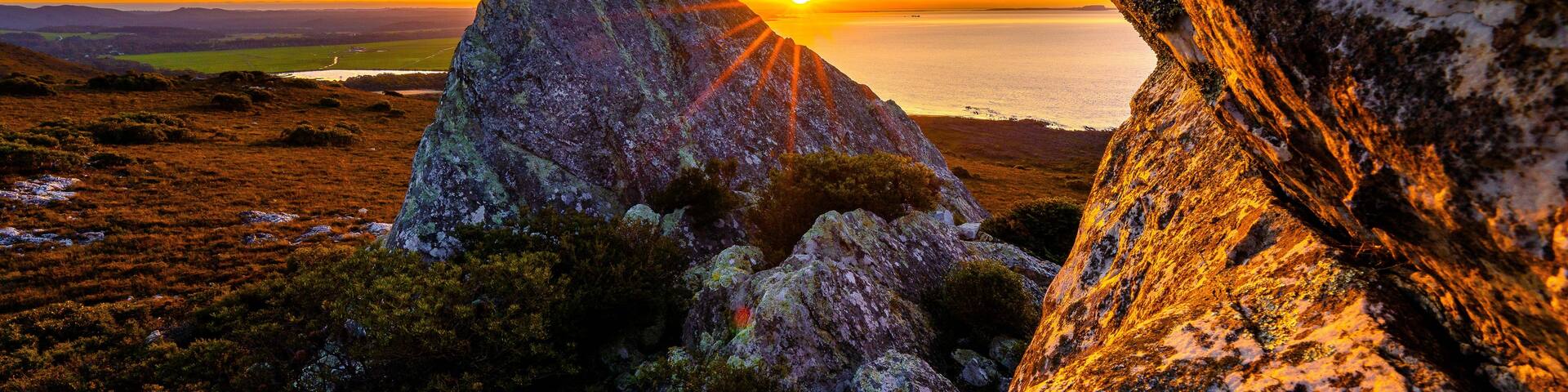 A sunset over a coastal landscape with prominent rock formations and a distant view of the sea.