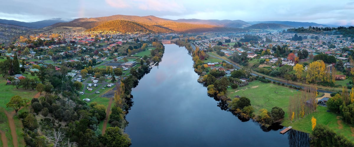 A river winding through a town with surrounding hills and autumn foliage.