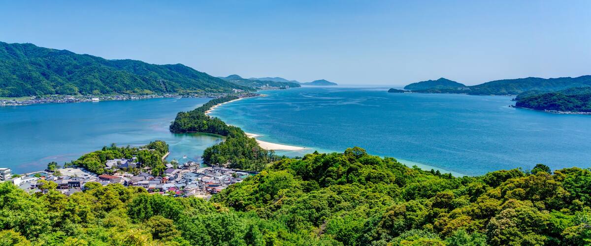A coastal landscape with a bay, a small town, and lush green hills.