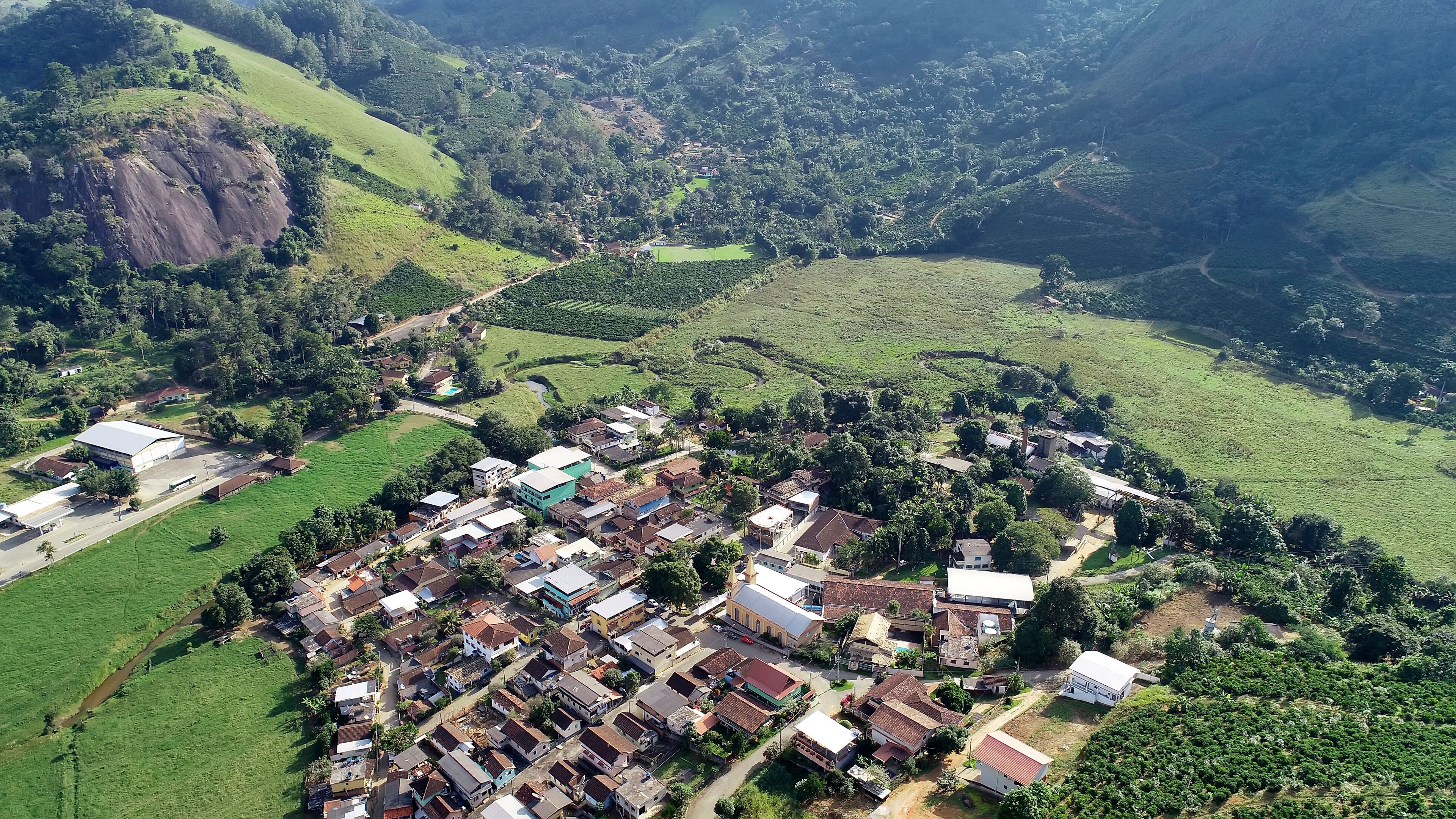 An aerial view of a rural village with houses, a church, and surrounding green fields and hills.