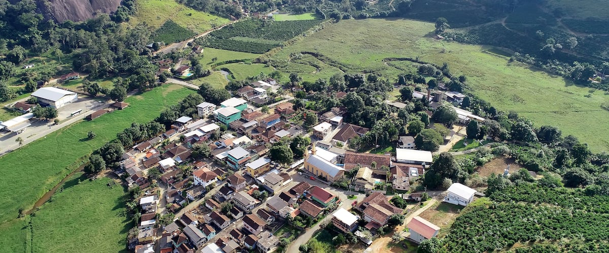 An aerial view of a rural village with houses, a church, and surrounding green fields and hills.