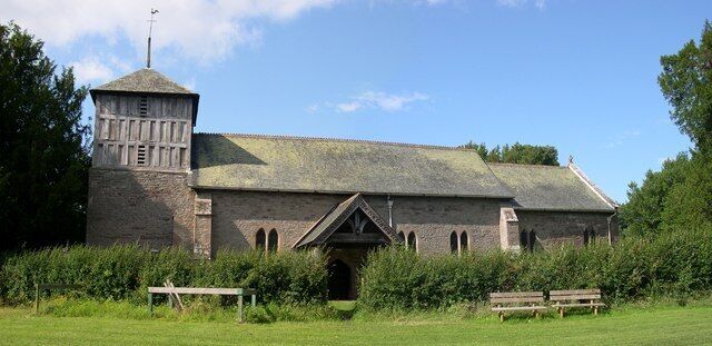 A historic stone building with a tower and arched windows, surrounded by greenery.