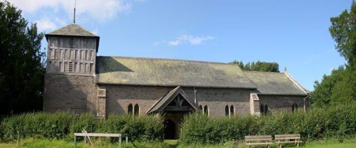 A historic stone building with a tower and arched windows, surrounded by greenery.