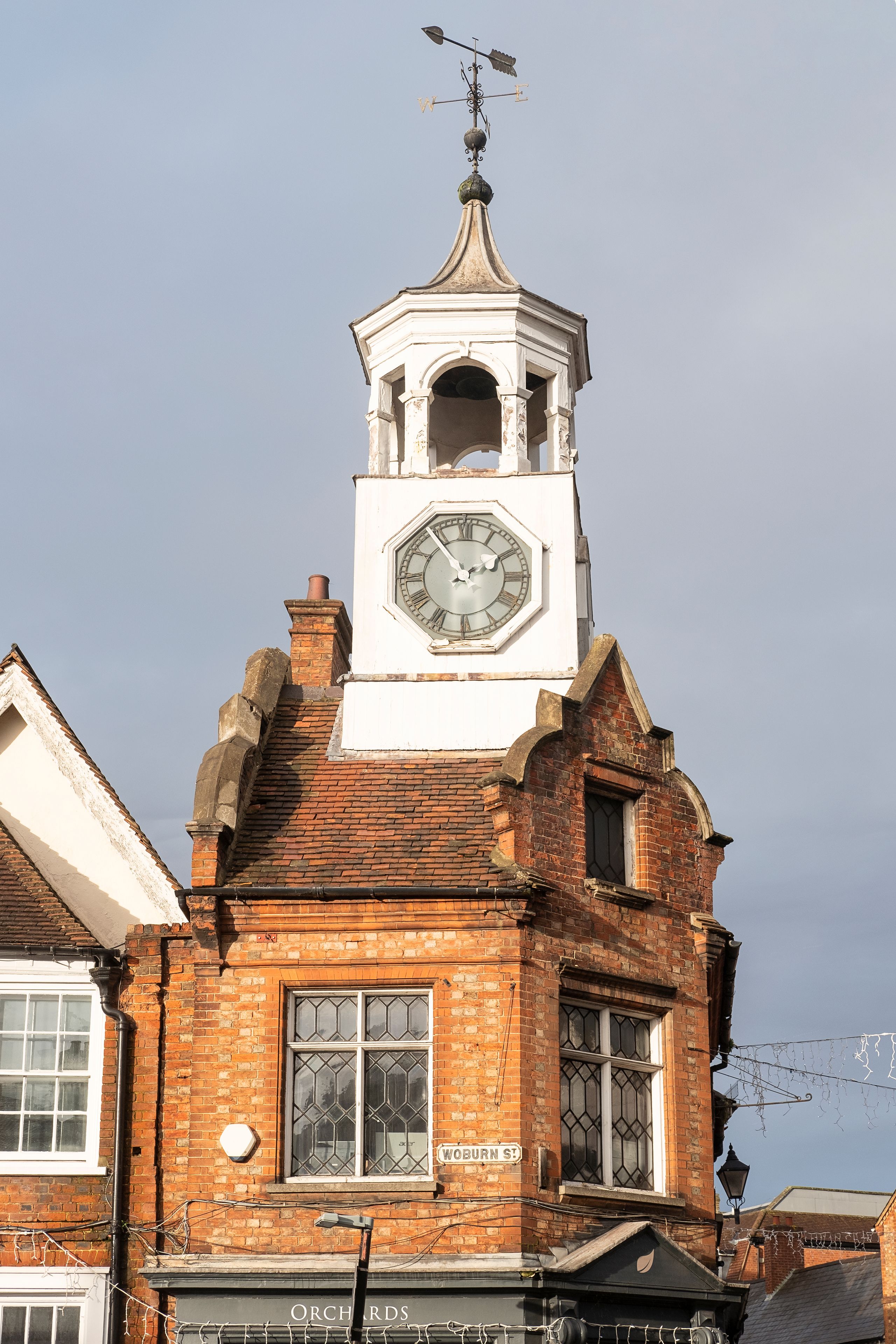 A historic building with a prominent clock tower, a weather vane, and a sign reading 'Woburn St.'