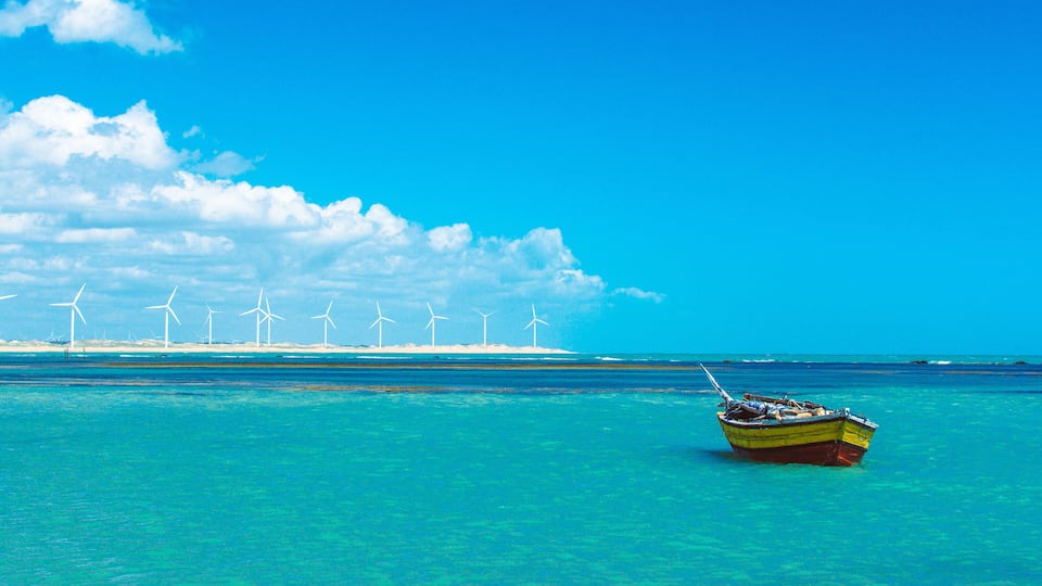 A boat on turquoise water with wind turbines in the background.
