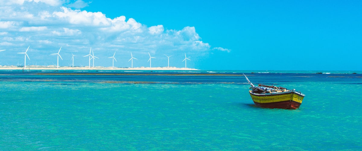 A boat on turquoise water with wind turbines in the background.
