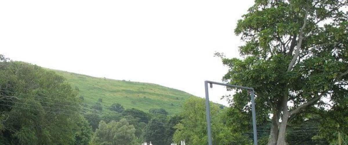 A rural landscape with a white house on a hill, a metal fence, and a stone wall.