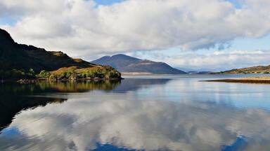 A calm lake with a mountain in the background and a cloudy sky.