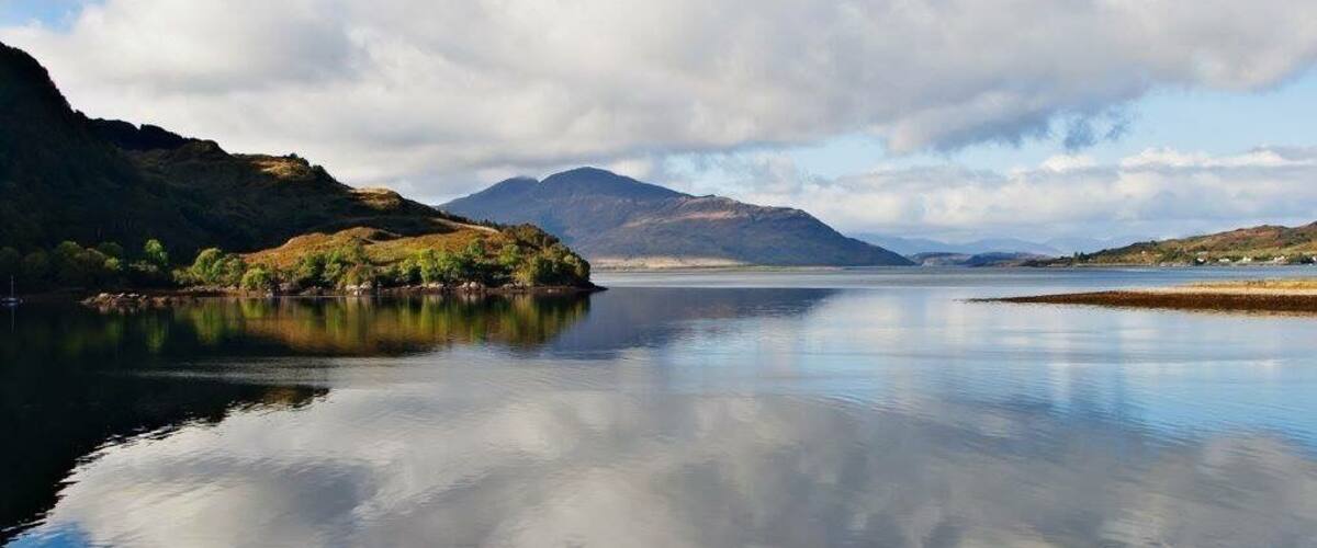 A calm lake with a mountain in the background and a cloudy sky.