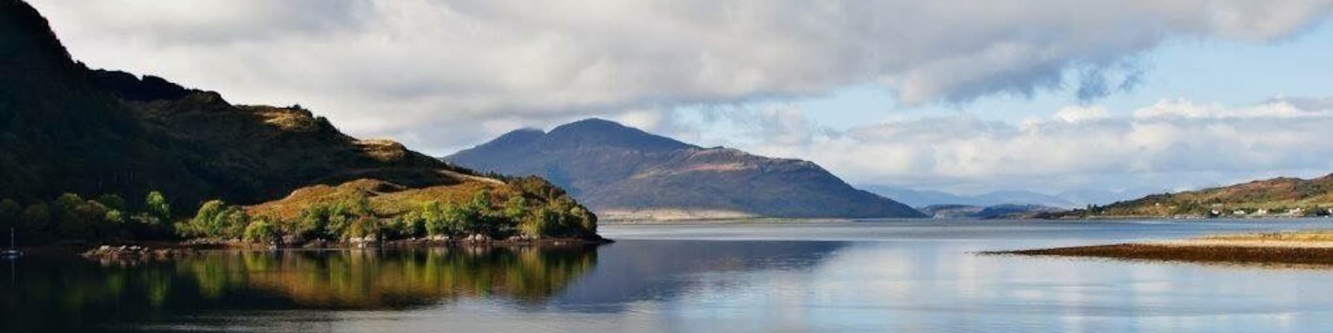 A calm lake with a mountain in the background and a cloudy sky.