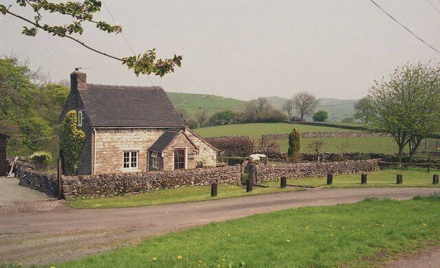 A stone house with a stone wall and a thatched roof, surrounded by a stone fence and a grassy field.