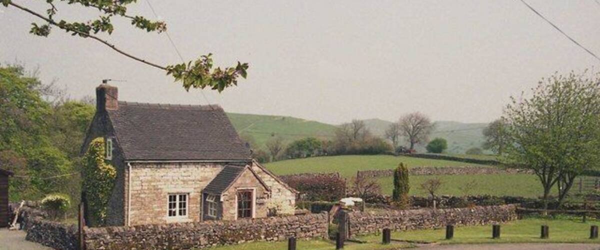 A stone house with a stone wall and a thatched roof, surrounded by a stone fence and a grassy field.