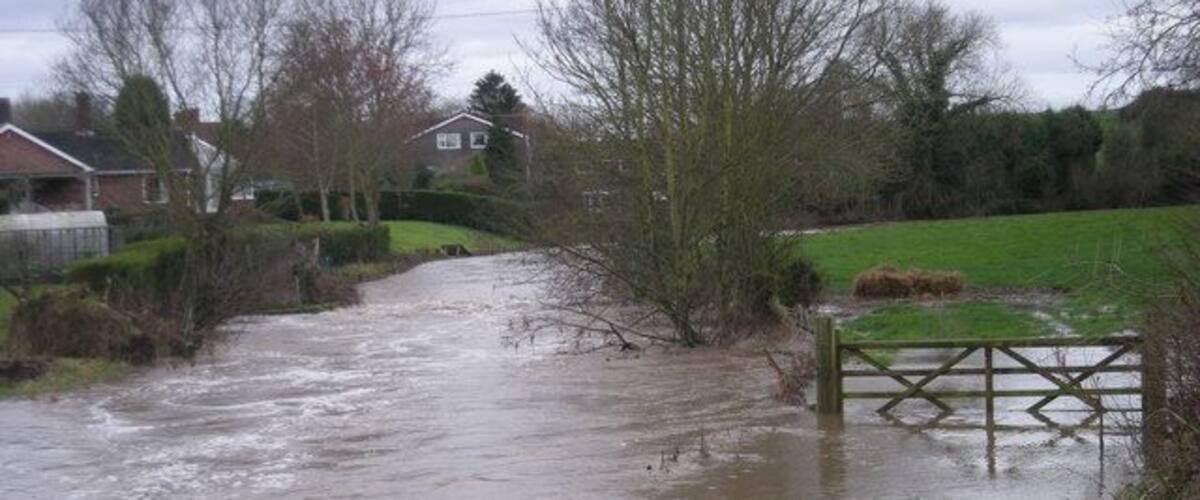 A flooded rural road with a wooden gate.