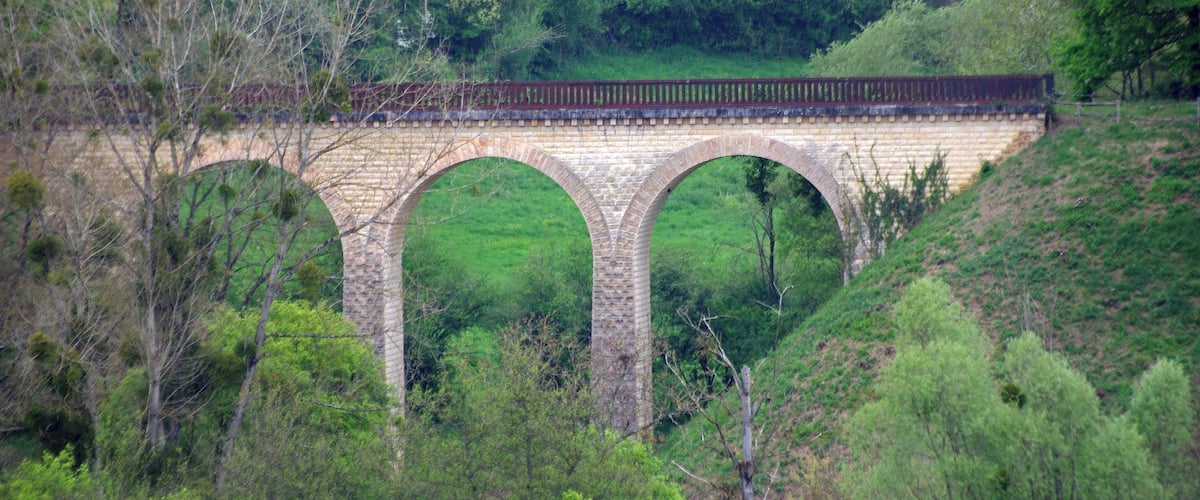 A stone bridge with three arches over a river, surrounded by lush greenery.