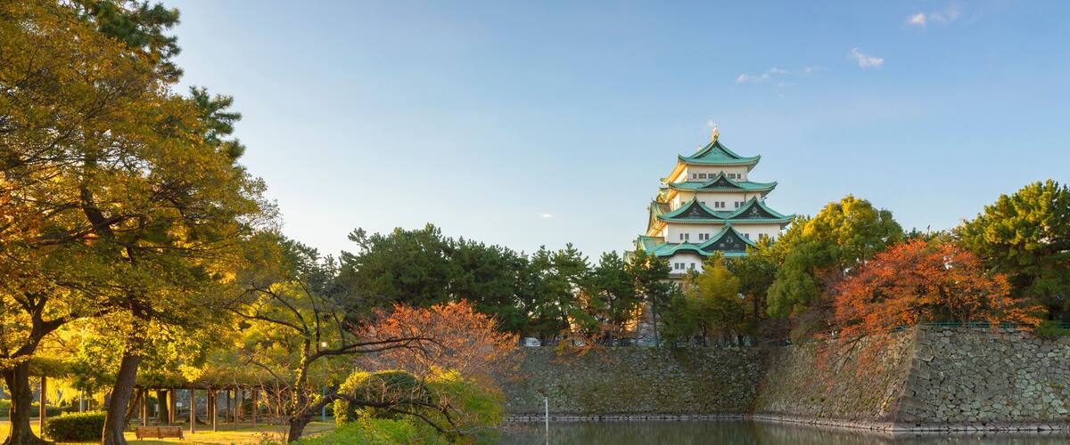 A traditional Japanese castle with a reflection in the water, surrounded by trees and a stone wall.