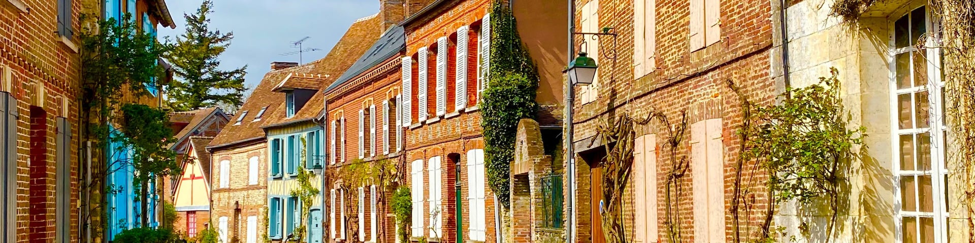 Eine enge Kopfsteinpflasterstraße, gesäumt von historischen Gebäuden, von denen einige mit blauen Fensterläden versehen sind, unter einem klaren Himmel.