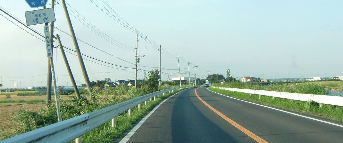 A rural road with a guardrail, utility poles, and a blue sign indicating a route number.