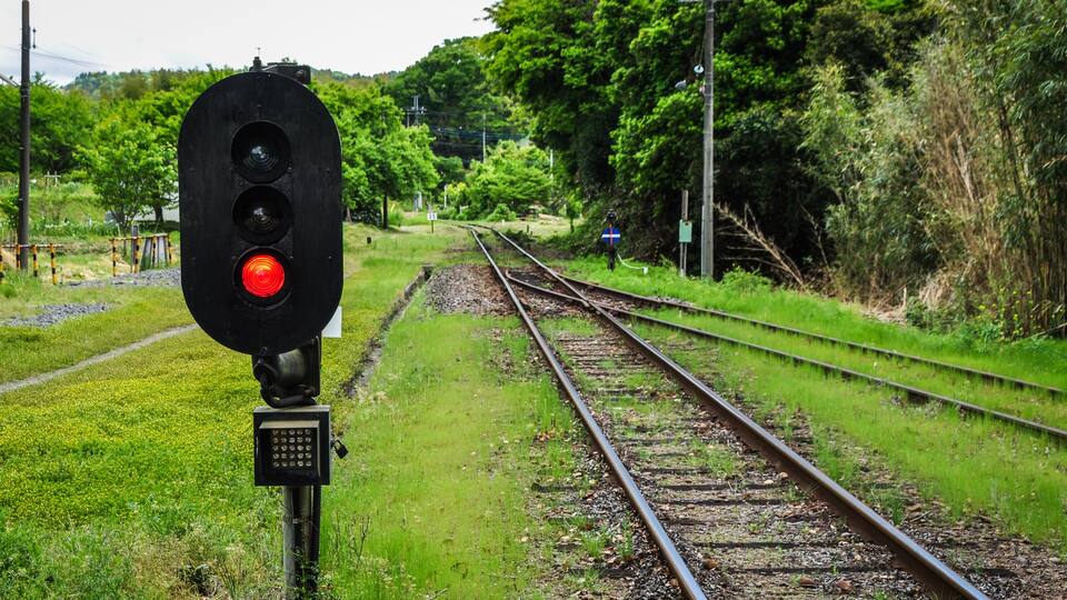 Railway tracks with a red signal light and a blue sign on the right.