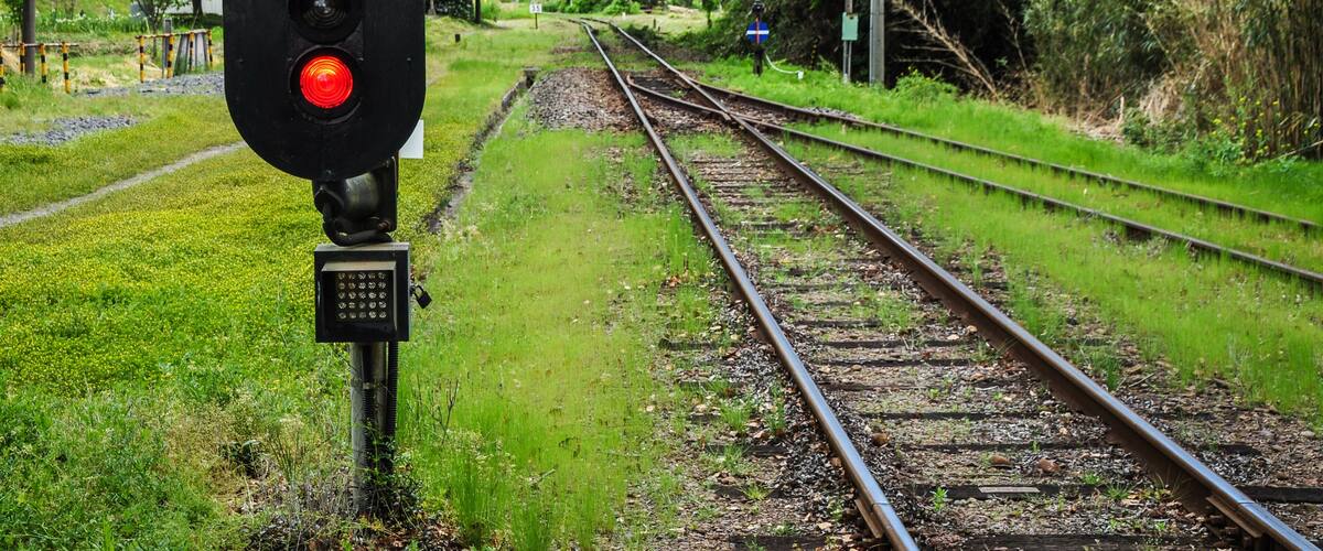 Railway tracks with a red signal light and a blue sign on the right.