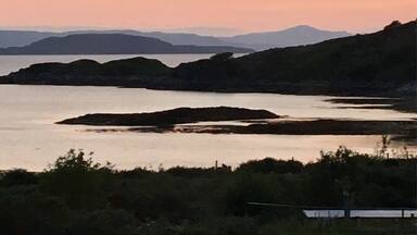 A coastal landscape with hills and a calm body of water during sunset.