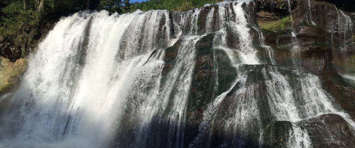 A waterfall cascading over rocky terrain surrounded by dense green forest.