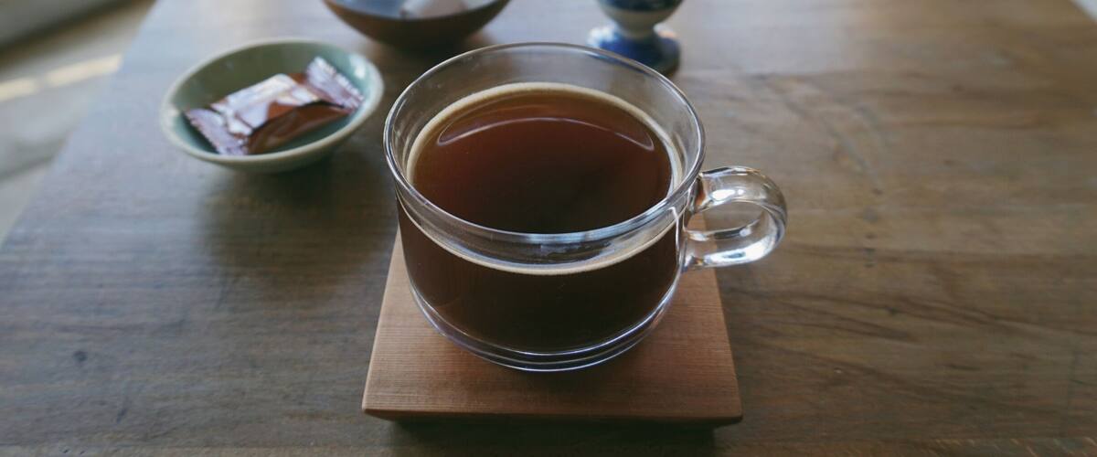 A glass of tea on a wooden table with a blue patterned cup and a small bowl in the background.