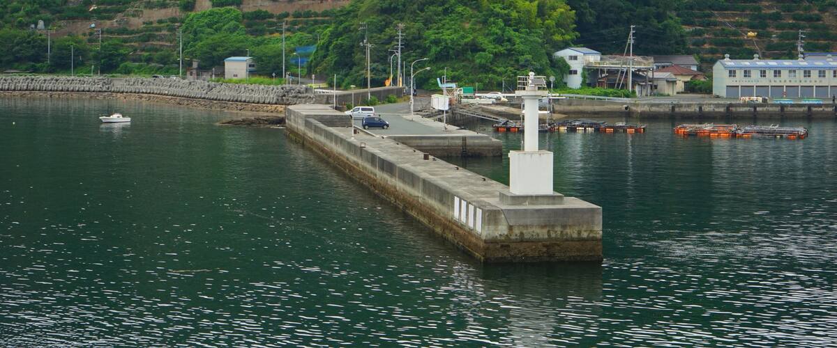 A harbor with a concrete pier, a small boat, and a hillside with terraced fields.