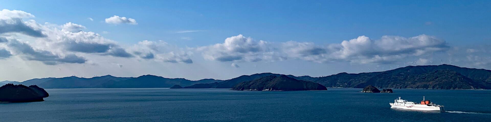 A clear blue sky, calm sea, and distant mountains.