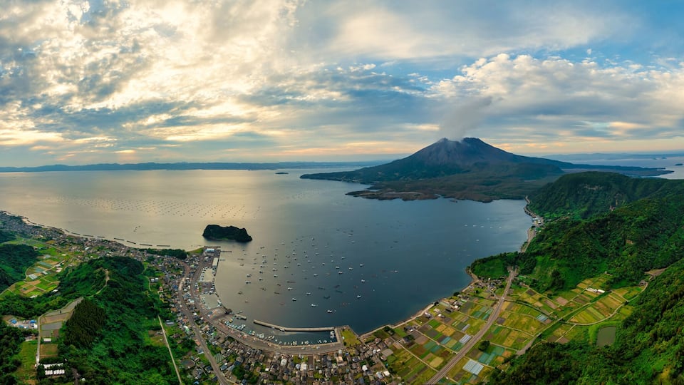 A coastal town with a large body of water, a mountain, and lush green hills.