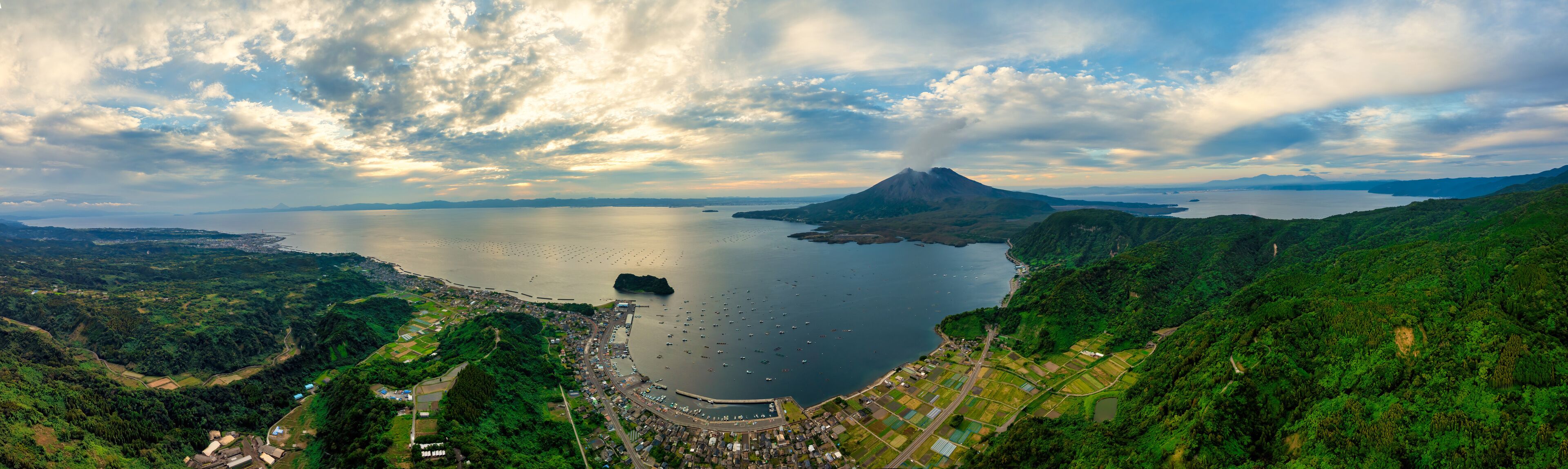A coastal town with a large body of water, a mountain, and lush green hills.